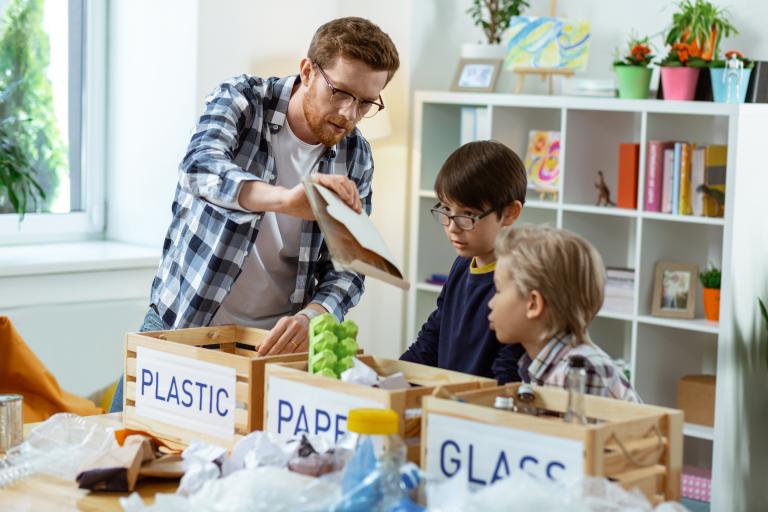 Three pupils sort recycled materials into boxes with help from a teacher.