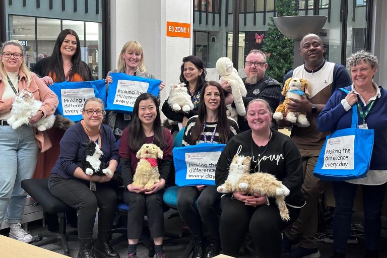 A large group of people gathered around inside an office, holding several robotic companion pets.