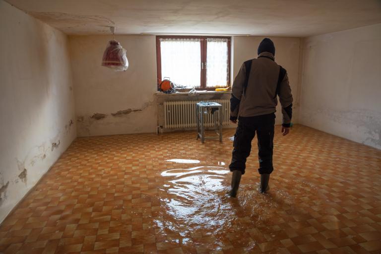 A man wades through a flooded and damaged house.