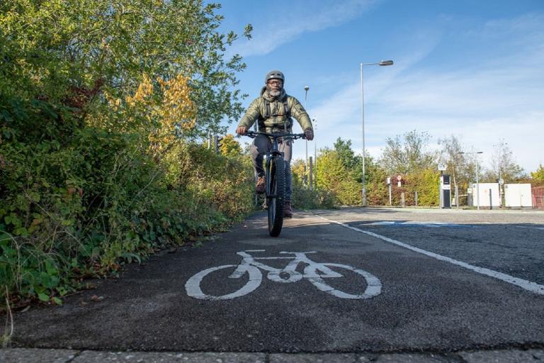 A man wearing a cycling helmet and green jacket riding a bicycle along a segregated cycle lane.