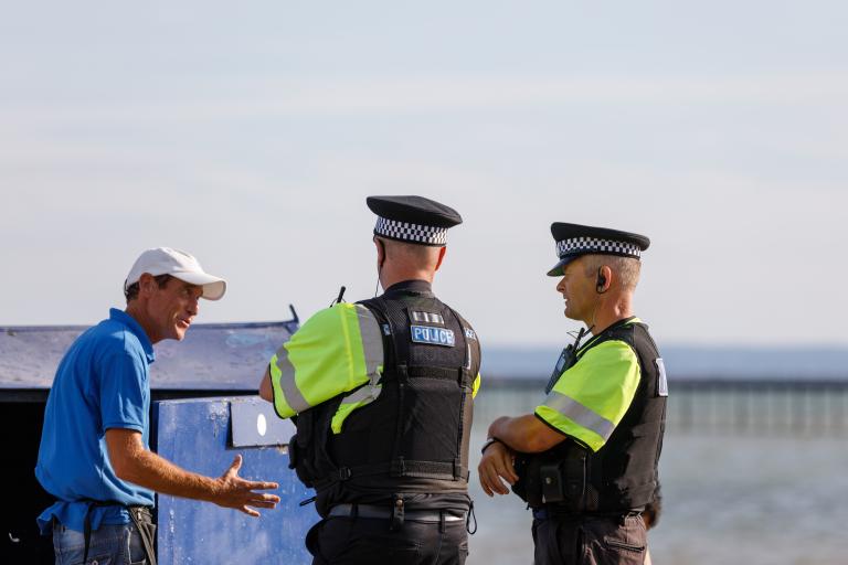 Police officers speak with an older man in front of a bridge across the water in Southend-on-Sea.