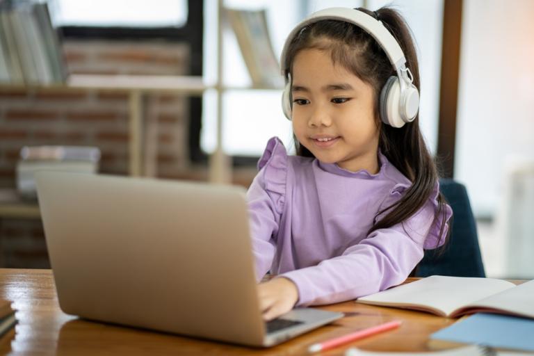 Young Asian female student wearing headphones studying watching video conference, laptop computer, online distance learning at home