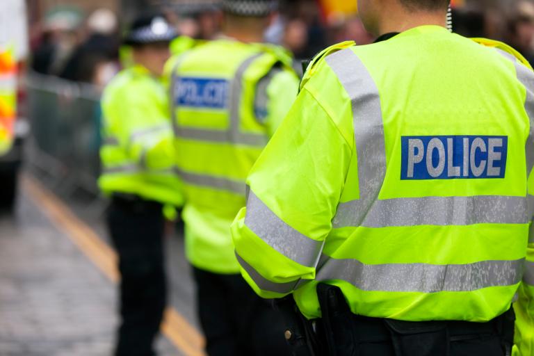 Row of police men and women with back of yellow high-vis jackets facing camera.jpg