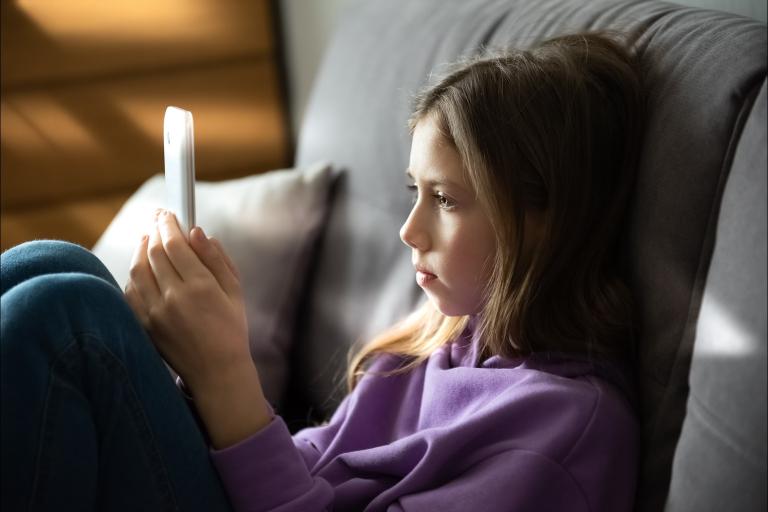 A young girl sitting holding a phone. She is looking at the screen.