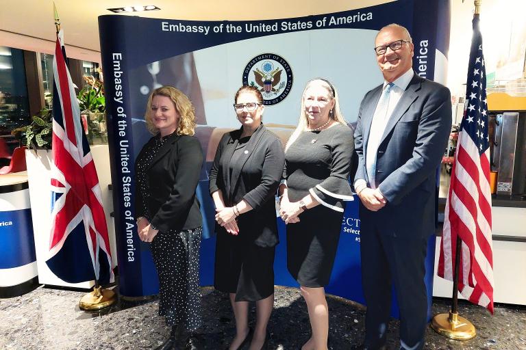 Four people in smart clothes standing in front of a banner.