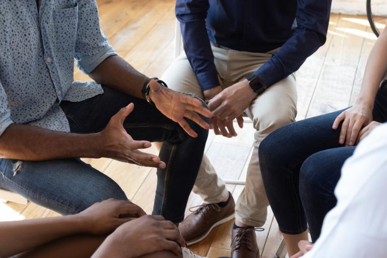 Close-up of people sit in a circle sat in a circle in discussion.