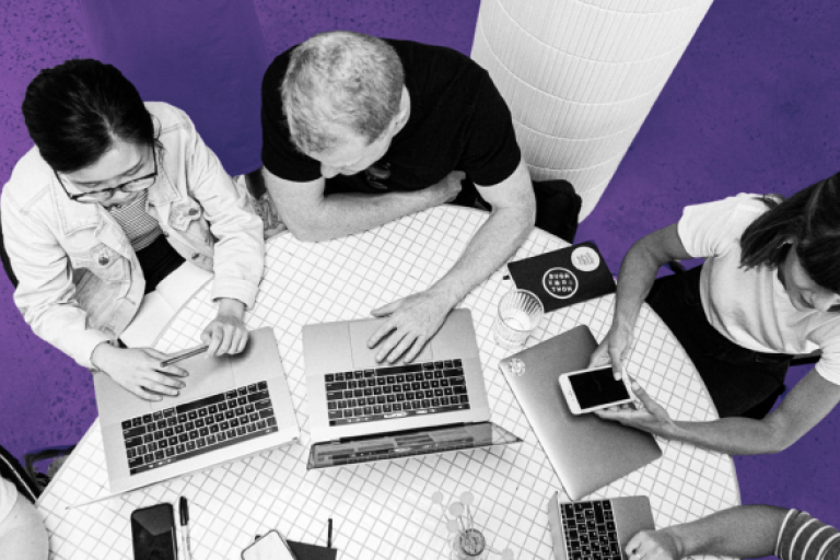 three people gathered around a desk with laptops on, top view looking down