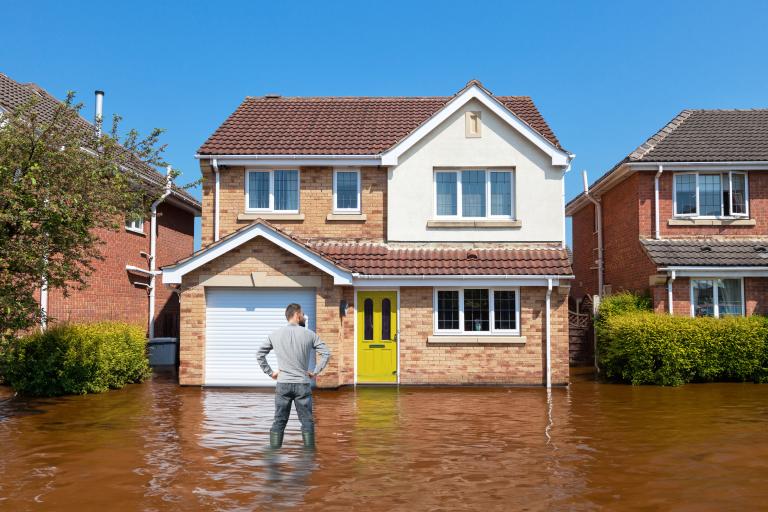 AI-generated image of man in wellies up to his knees in flood water in front of a house