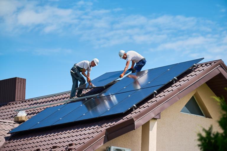Two men installing solar panels on the roof of a house.