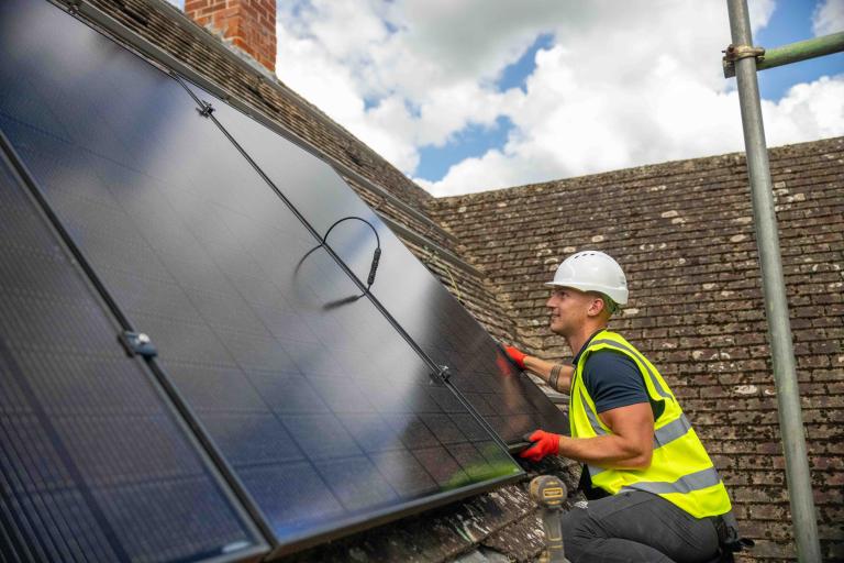Man in high visibility jacket with white safety helmet on a roof fitting solar panels