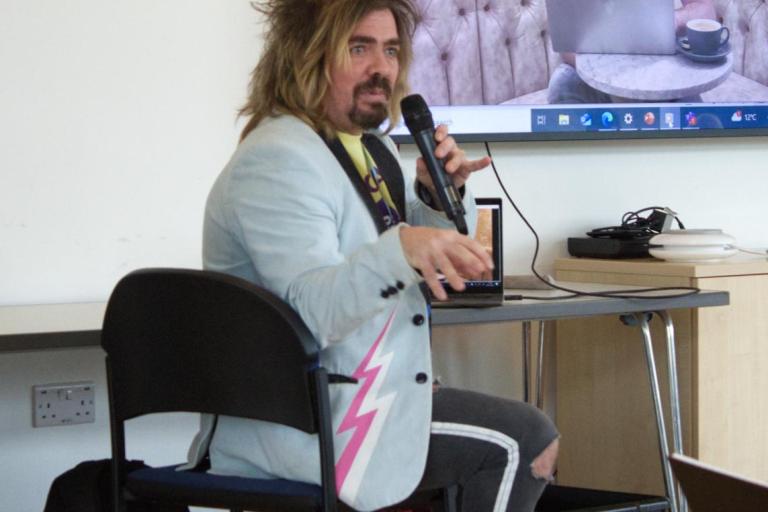 Man talking on microphone with large screen in background
