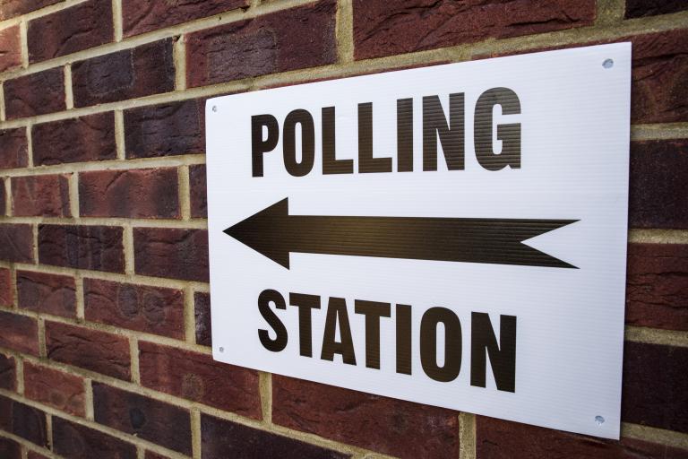 Polling station sign mounted on a brick wall.