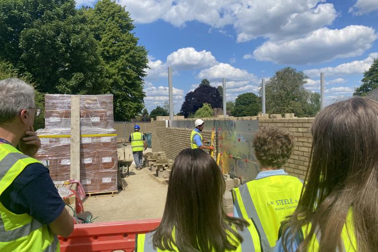young people in hi-vis watching a man build a wall
