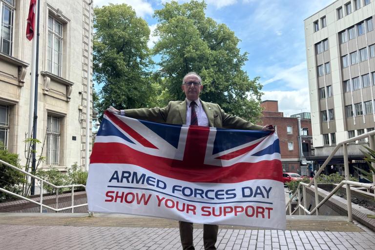 Councillor Louis holds out a British armed forces flag atop the steps of County Hall.