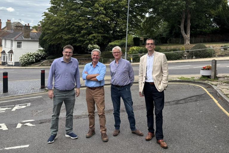 Four men standing on in front of a road of houses.