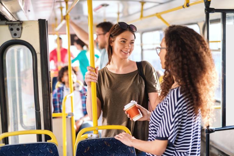 Two women standing inside a bus holding on to yellow handrails.
