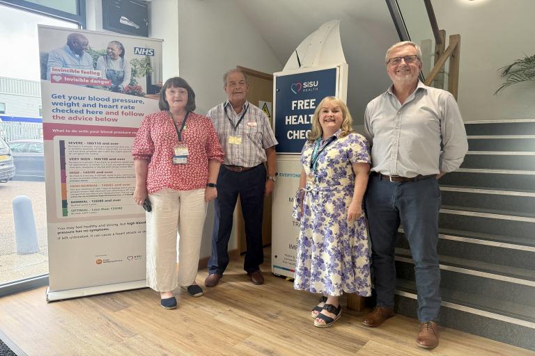 Councillor John Spence with colleagues visiting a digital health check station at Baker Labels.  A group of four people are standing in front of the station.