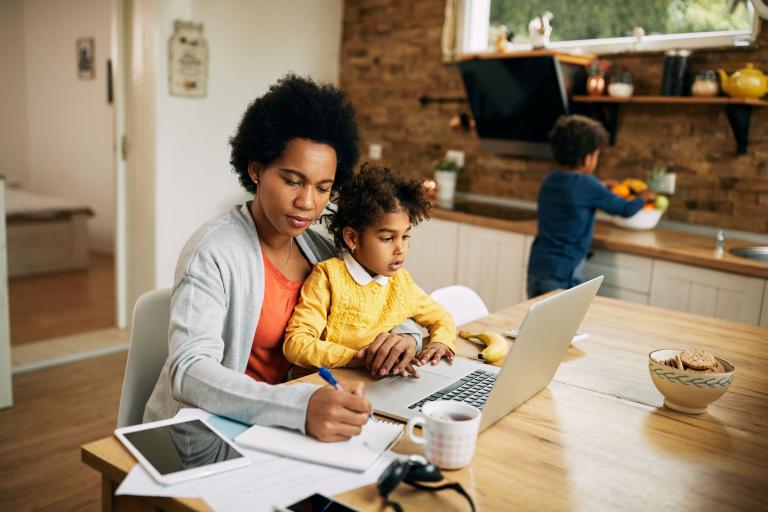 Women working on a laptop at the table with a child on her lap.