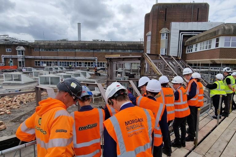 Group of students in hi-vis with backs turned to camera as they look out over a construction site.