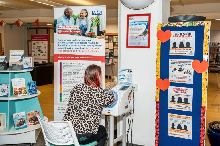 A blood pressure monitor. A lady is sitting at the monitor taking her blood pressure.