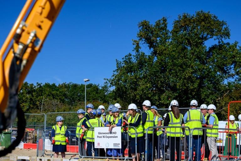 A group of people wearing hard hats and high-visibility jackets standing on a building site.
