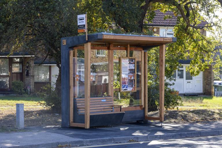 A bus shelter in a street with trees behind.
