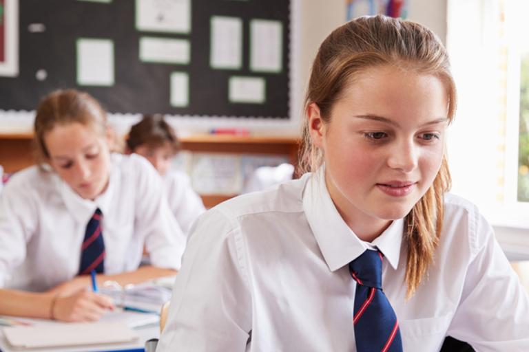 Two female teenage pupils in shirts and ties sat at desks looking at work