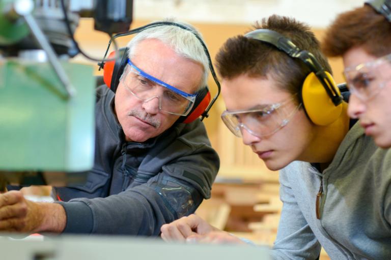Two apprentices being taught how to work machinery by a tutor.