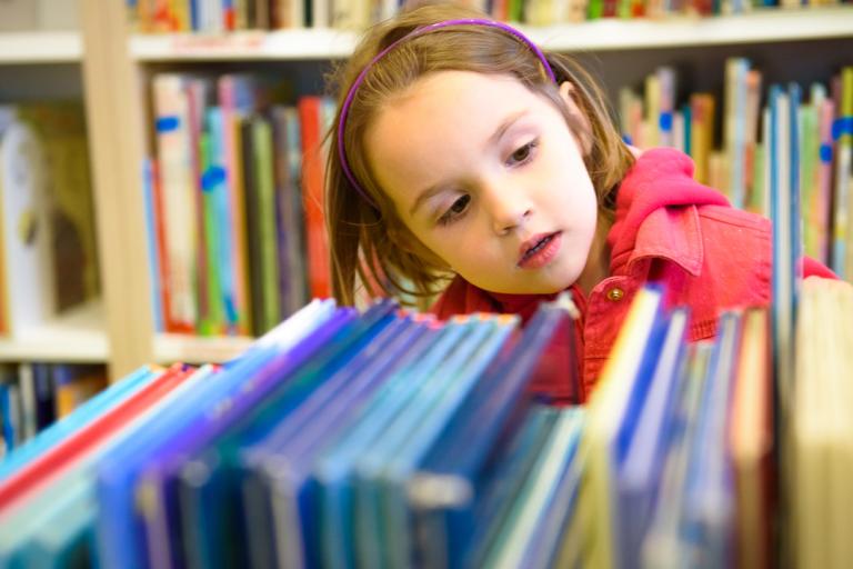 A young girl browsing some books on a library shelf.