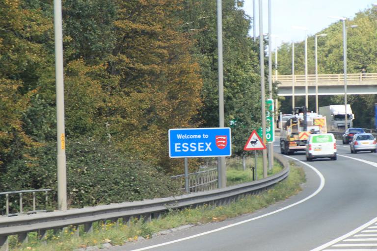 A Welcome to Essex road sign on the side of a busy road with cars and trucks on
