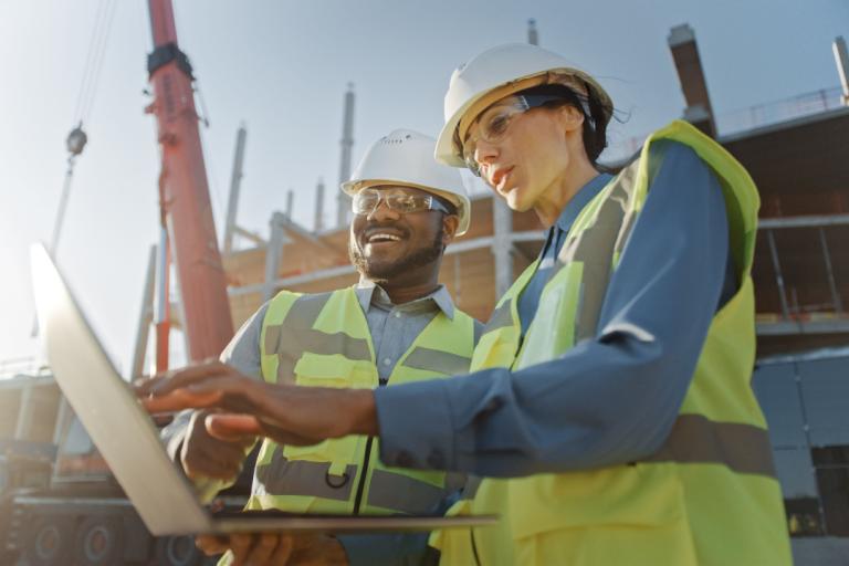 A man and a woman looking at a laptop whilst on a building site.