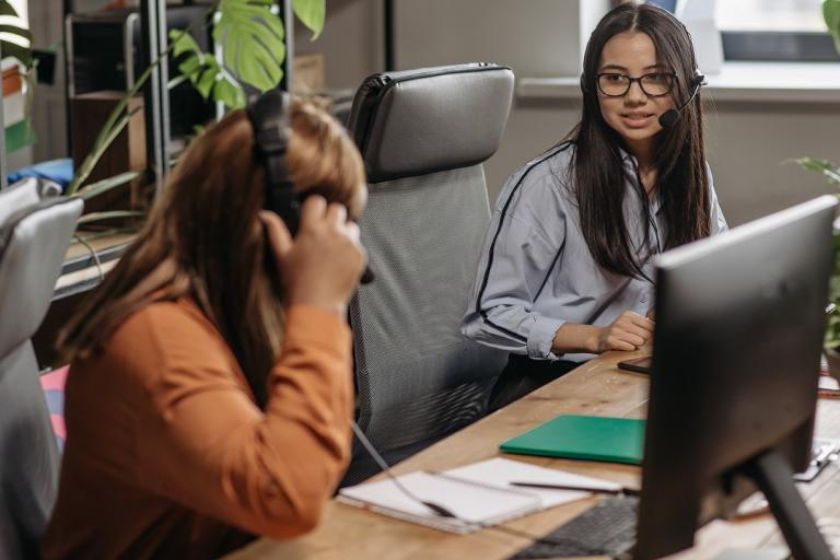 Two women with headsets at computers in an office