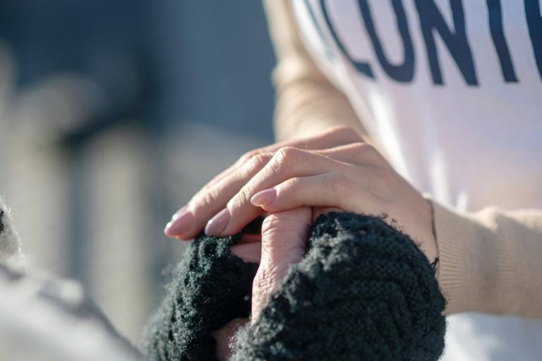 Close up of a homeless woman's hands on gloves being held by a caring woman's hands