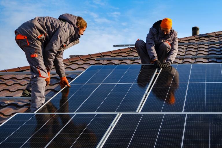 Two men working to fit some solar panels to a roof.