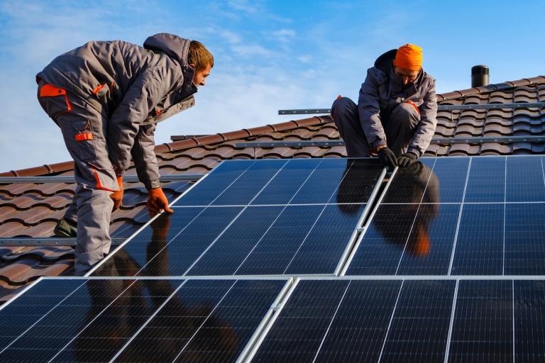 Two men working to fit some solar panels to a roof.