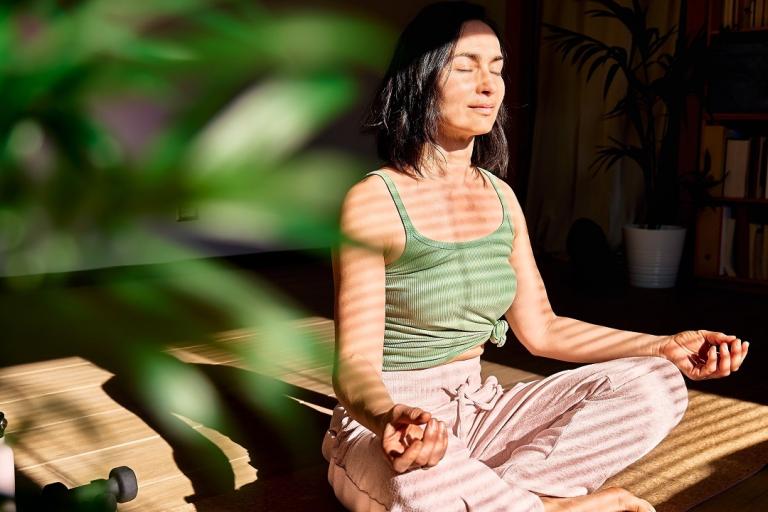 Woman practicing yoga and meditation at home sitting in lotus pose on yoga mat.