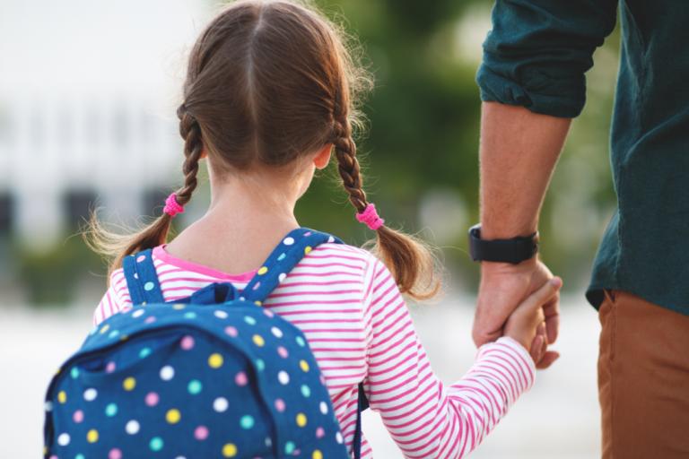 A young girl walks to school holding her father's hand. 