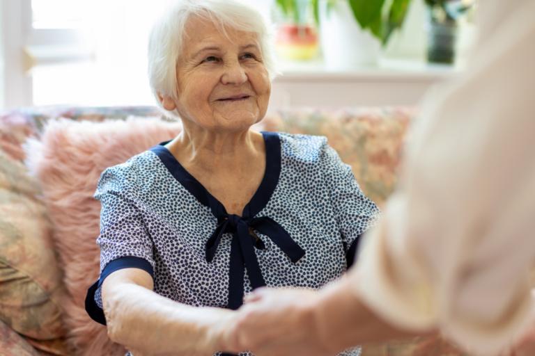 An elderly woman holding hands with a carer.